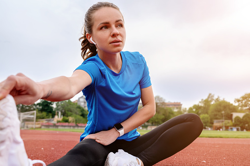 Athlete woman with wireless earphones doing stretching exercise after running training.