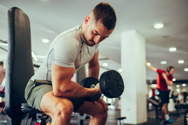 istock A fit sportsman doing exercise for biceps with a dumbbell while sitting in a gym. 1487570039