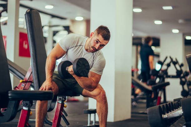 istock A strong sportsman with big muscles is pumping biceps in a gym while sitting on an exercise machine and making eye contact. 1487570048