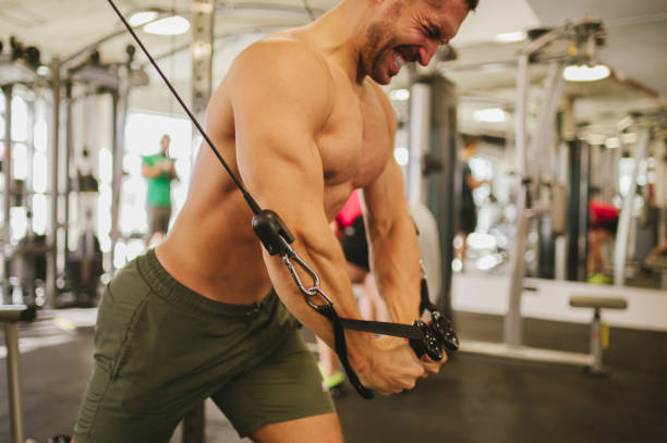 istock Side view of a strong sportsman pulling weights on a cable machine in a gym. 1487570061