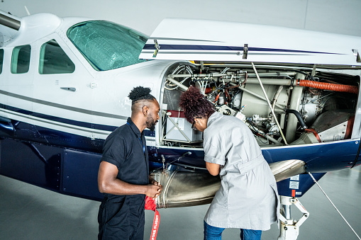 Airplane mechanic looking to his coworker work in the airport hangar