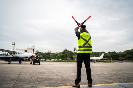 Man signaling the pilot with marshalling wands on airport