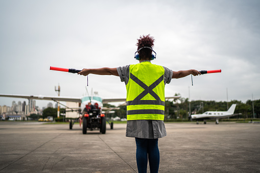 Woman signaling the pilot with marshalling wands on airport