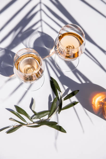 Drinking rose wine glasses on white table with olive branch and palm leaf shadow stock photo