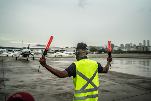 Man signaling the pilot with marshalling wands on airport