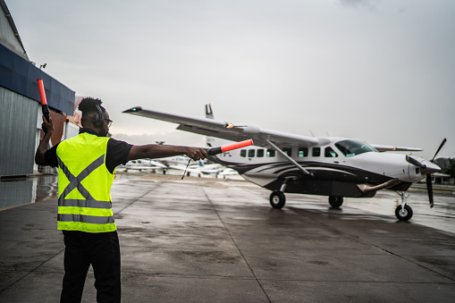 Man signaling the pilot with marshalling wands on airport