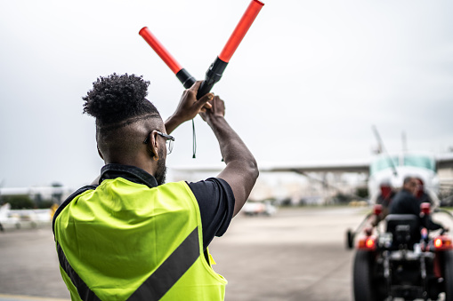 Man signaling the pilot with marshalling wands on airport