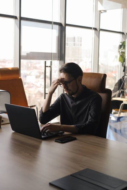 istock tired manager holding his head behind a laptop in the office 1487578004