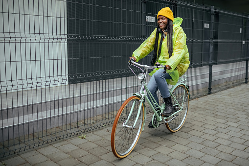 Cheerful woman riding bicycle in raincoat.