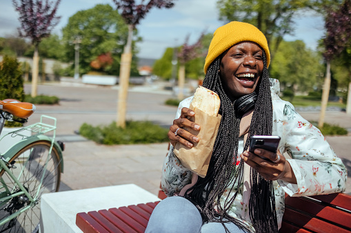 Woman is sitting on a bench with coffee and a sandwich