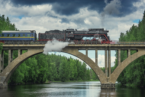 Retro steam train moves above the river at summer day.