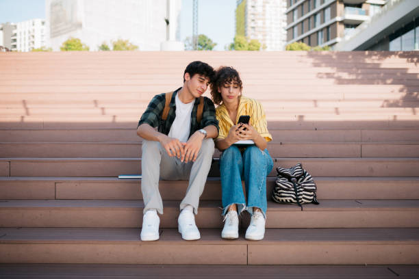 istock Two university students sitting on the steps outside using a smart phone 1487587101