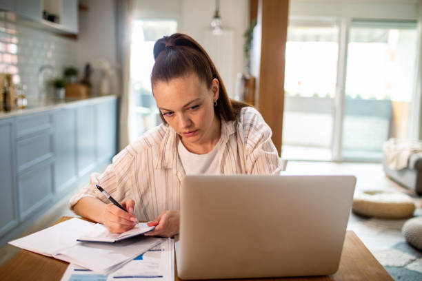 istock Young woman going over her finances at home while using her laptop 1487587247