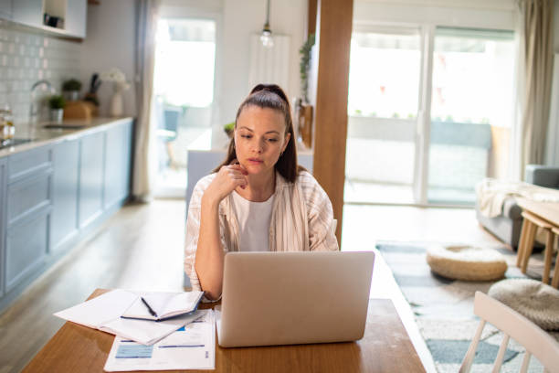 istock Young woman going over her finances at home while using her laptop 1487587303