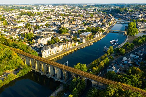 General aerial view of Laval town overlooking arched railway bridge across Mayenne River on summer day, France