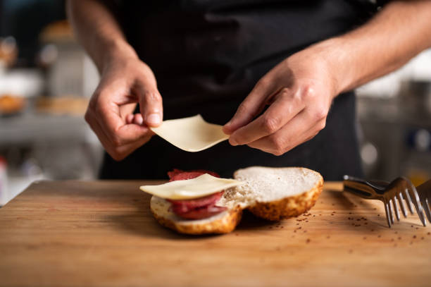A male chef prepares a sausage and cheese sandwich