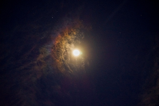 full moon against dark night sky as iridescent clouds float by