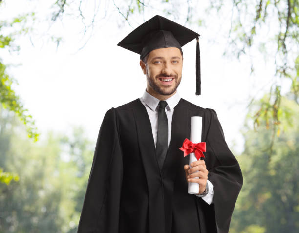 istock Male graduate studend with a diploma standing outdoors 1487619547