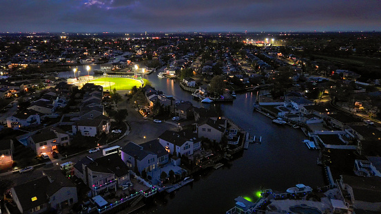 Wealthy luxury town with many houses and lights based on sea channel banks. One source of light is a green baseball diamond where amateur team baseball training. Oceanside, New York, Long Island. Night aerial view