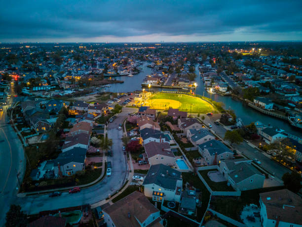 Illuminated waterside settlement in Oceanside, New York at sunset. Illuminated public community stadium in the center. Aerial view