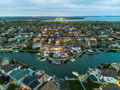 Small illuminated town on sea channel bank with boats and yachts on piers against cloudy sky, twilight in Nassau County, New York