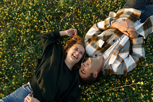 Top view of relaxed young couple lying together on green grass with eyes closed. Relationships and love concept.