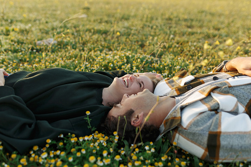 Side view of relaxed young couple lying together on green grass with eyes closed. Relationships and love concept.