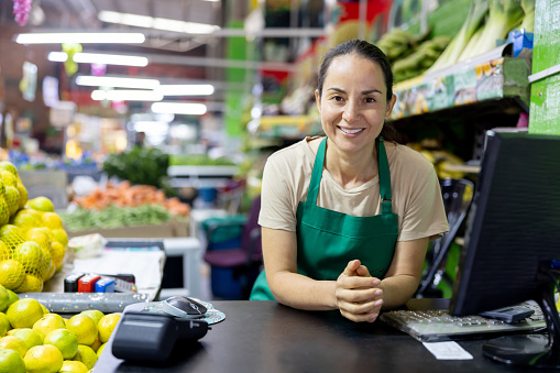 Happy Latin American cashier working at a supermarket and looking at the camera smiling