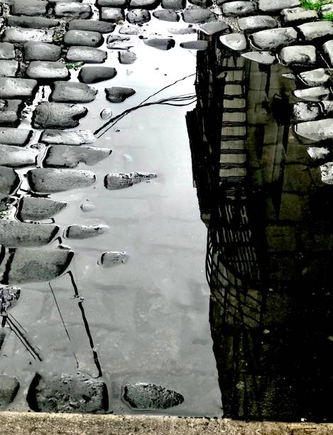 Rain Puddle on Cobblestone Streetm A big dip on a drenched historic cobblestone street became a receptacle for a dirty dark puddle and a reflecting pool for a building and utility wires during a rainstorm in Hoboken, New Jersey. drenched stock pictures, royalty-free photos & images