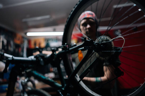 plan recadré détaillé d’un mécanicien méconnaissable réparant un vélo à l’aide d’un outil spécial travaillant dans un atelier de réparation de vélos avec un intérieur sombre. - cycling bicycle occupation men photos et images de collection