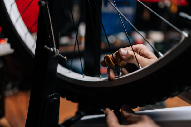 plan recadré en gros plan d’un mécanicien méconnaissable vérifiant une roue de vélo avec une clé à rayons de vélo travaillant dans un atelier de réparation de vélos avec un intérieur sombre. - cycling bicycle occupation men photos et images de collection