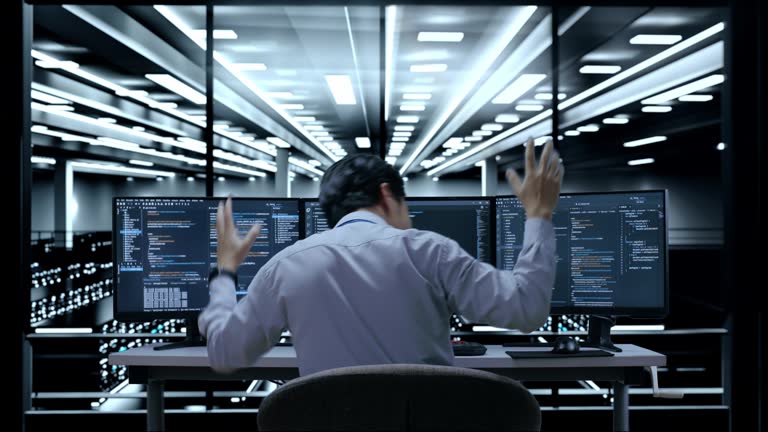 Back View Of Asian Male Programmer Celebrating Succeed Writing Code By Desktops Using Multiple Monitors Showing Database On Terminal Window In The Server Room