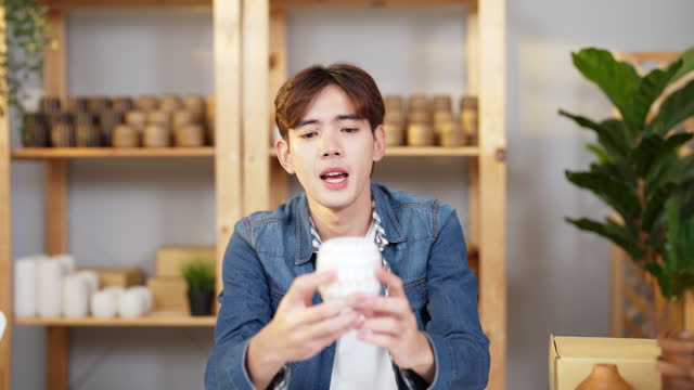 Portrait of Asian young adult man giving a presentation about vase product and showing the goods in front of camera.