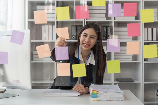 Happy business female planning ideas on a glass wall with colorful sticky notes inside a office.