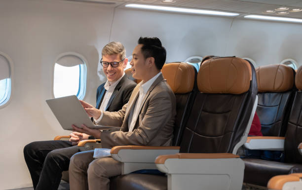 istock Two businessmen using laptop and working together in airplane cabin. 1487656443