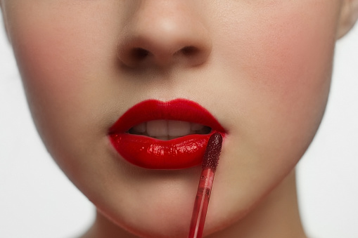 Female painting her lips with red lipstick, close-up of lips.