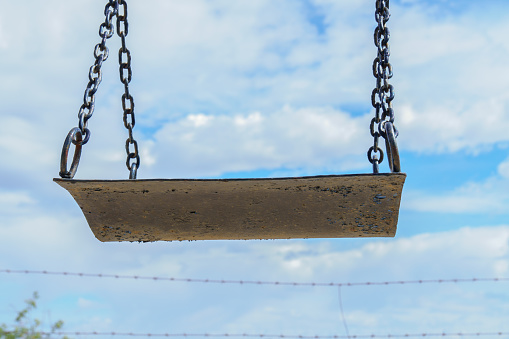 close-up of a rusty swing with a cloudy sky and barbed wire in the background