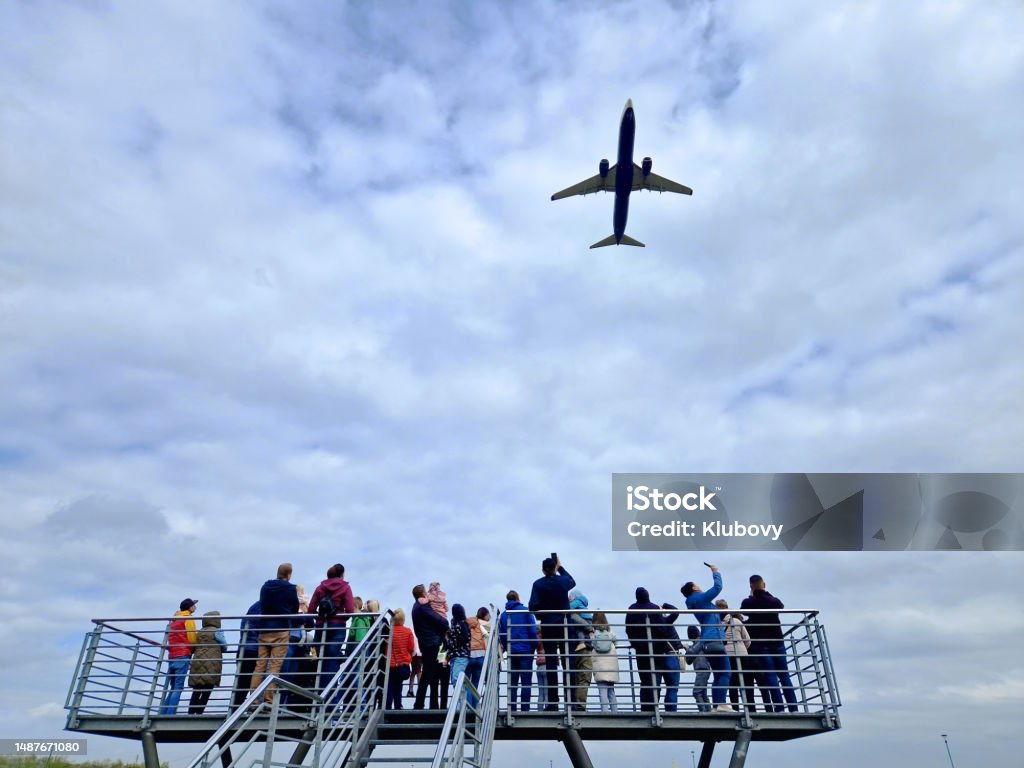 Group of people watching an airplane taking off. Group of unrecognizable random people standing on the observation platform, watching an airplane taking off. Photo taken in a public area outside the airport. Airplane Stock Photo