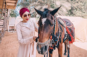 In the dusty desert, a girl with a flowing dress gently leads her Arabian horse, their bond unbreakable and their journey endless.