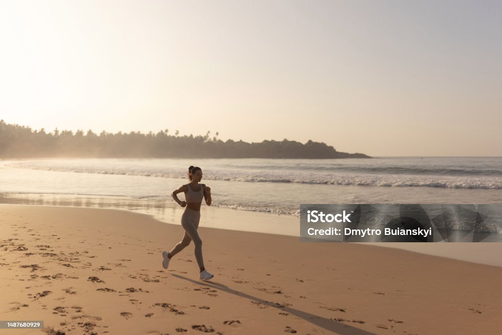 Silhouette of Runner Woman Alone at Early Sunset Outdoors on the Beach Silhouette of the woman running alone at beautiful sunset on the beach. Summer sport and freedom concept. Athlete training outdoors. High quality photo Cardiovascular Exercise Stock Photo
