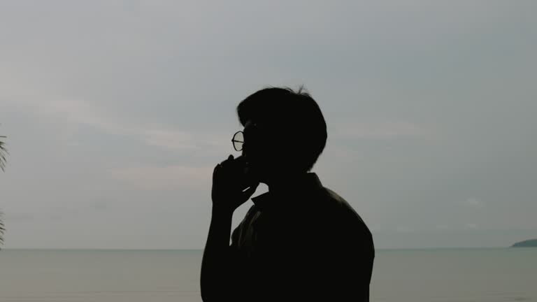 Transgender man standing at the beach and talking on phone.