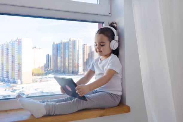 istock A girl using digital tablet reading electronic book sitting on the windowsill. 1487684776