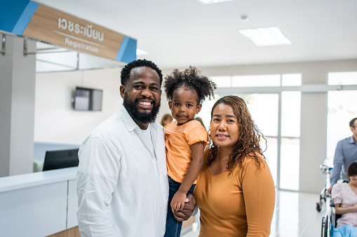 Portrait of African family patient stand in corridor at hospital ward. Attractive couple and daughter walking in hallway waiting on line que to receive medicine in pharmacy counter at medical center.
