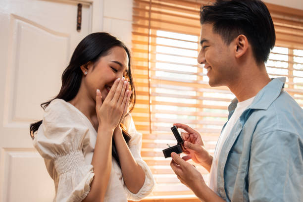 asian romantic man making surprise proposal of marriage to girlfriend. attractive young male and proposing to beautiful happy woman, with wedding ring enjoying surprise engagement in kitchen at home. - fästfolk bildbanksfoton och bilder