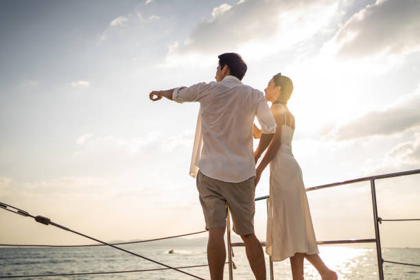 bella coppia asiatica che beve champagne mentre fa festa in yacht. attraente uomo e donna che escono, celebrando il viaggio di nozze anniversario mentre navigano in catamarano durante il tramonto estivo. - lake summer beach nautical vessel foto e immagini stock