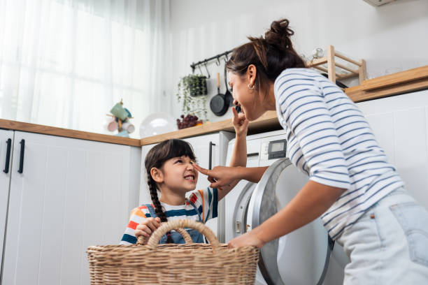 mãe caucasiana bonita ensinando filha pequena lavar roupas sujas. adorável menina menina bonita ajuda e aprender com a mãe dos pais para colocar a roupa no aparelho de lavar em casa. doméstica-housekeeping. - stereotypical housewife little girls family domestic kitchen - fotografias e filmes do acervo