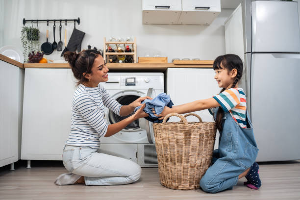 mãe caucasiana bonita ensinando filha pequena lavar roupas sujas. adorável menina menina bonita ajuda e aprender com a mãe dos pais para colocar a roupa no aparelho de lavar em casa. doméstica-housekeeping. - stereotypical housewife little girls family domestic kitchen - fotografias e filmes do acervo