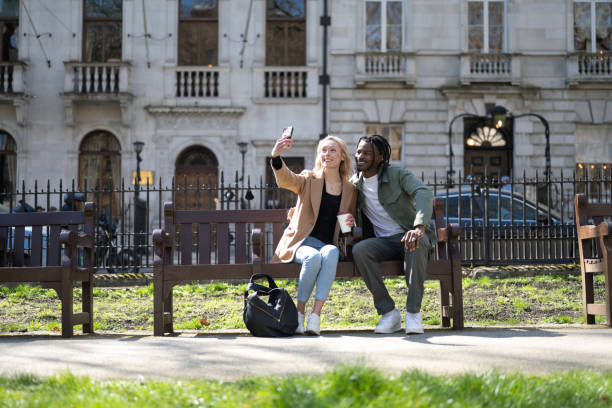 istock Couple sitting on London park bench taking a selfie 1487689452