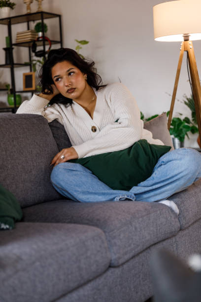 Young woman sitting on the sofa, head in hand, contemplating life's problems stock photo