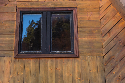 Window in a wooden house. wooden house with window frame. Old wooden house in the village, Wood board background, texture. Window with glass and frame wood and wooden home in rural or countryside.